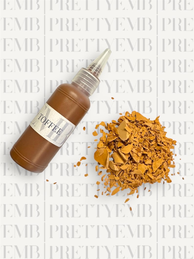 May include: A brown glass bottle with a white label that says "TOFFEE" and a clear plastic dropper top. The bottle is sitting on a white surface with a pile of broken, orange-brown pieces of toffee.