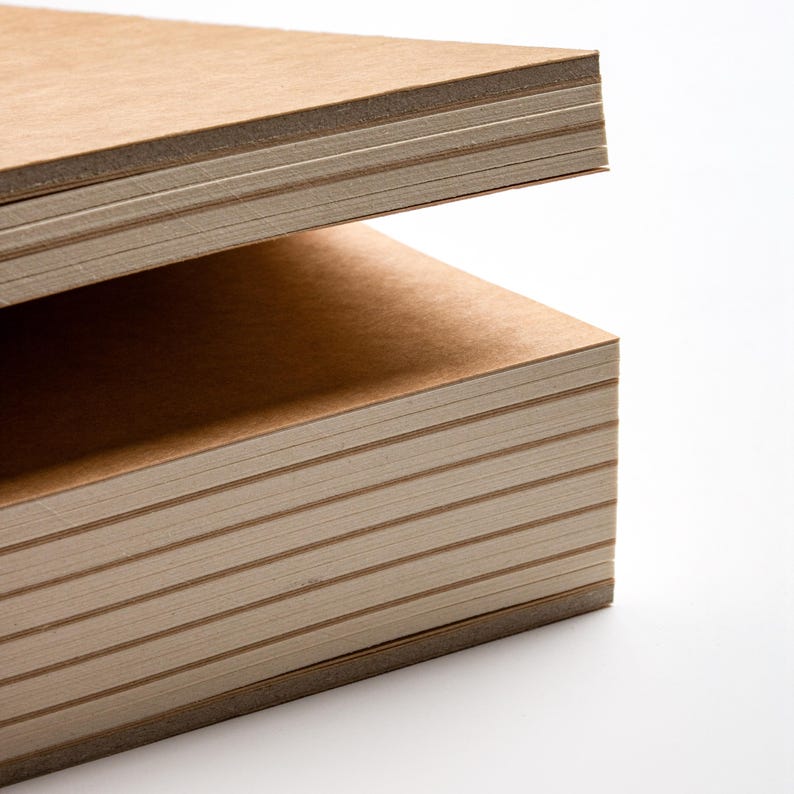 Peut inclure: Gros plan sur deux piles de blocs-notes rectangulaires brun clair. Les blocs-notes ont un aspect rugueux et textur&eacute; et sont empil&eacute;s les uns sur les autres sur un fond blanc. Les bords du papier sont visibles, montrant les feuilles individuelles.