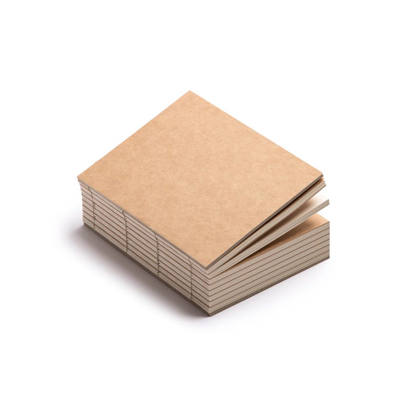 Peut inclure: Une pile de petits cahiers carr&eacute;s avec des couvertures en papier kraft brun. Les pages de couleur cr&egrave;me sont reli&eacute;es par des coutures visibles le long de la tranche. Le cahier sup&eacute;rieur est l&eacute;g&egrave;rement ouvert, r&eacute;v&eacute;lant les pages int&eacute;rieures.