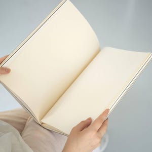 basenotes 2333 sketchbook opened on lap showing cream-toned acid-free pages and hand-stitched spine.