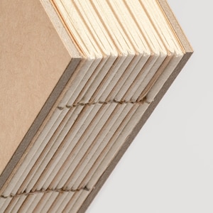 May include: Close-up of a handmade journal with a brown cover and cream-colored pages. The pages are sewn together, and the edges are visible. The journal is angled, showing the binding and the texture of the paper.