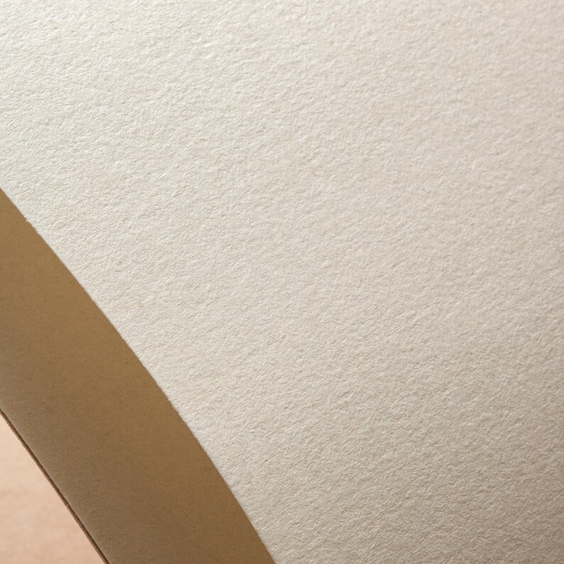 Peut inclure: Gros plan sur une surface de papier textur&eacute; blanc cass&eacute; avec un bord diagonal beige. Le papier a une finition l&eacute;g&egrave;rement rugueuse et mate, sugg&eacute;rant qu'il peut convenir &agrave; l'&eacute;criture ou au dessin. L'image met en &eacute;vidence la texture et la couleur du papier.
