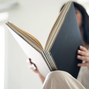 Person holding a basenotes 2333 sketchbook with a black cover, showing exposed spine and layered stitching.