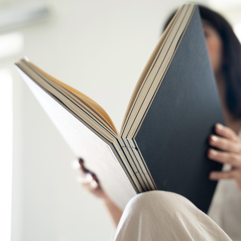 Person holding a basenotes 2333 sketchbook with a black cover, showing exposed spine and layered stitching.