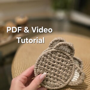 May include: A round, beige crocheted coaster with small, rounded ears at the top, featuring a textured, woven pattern. The text "PDF & Video Tutorial" is overlaid on the image, indicating the availability of instructional content for this item.