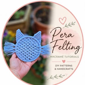 Op de afbeelding: Een lichtblauwe macramé kattenonderzetter met franjes, vastgehouden in een hand. De onderzetter heeft een cirkelvormige basis met kattenoren. De afbeelding bevat ook de tekst "Pera Felting" en "Macrame Tutorials".