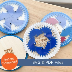 May include: Three blue and white plastic spin art templates with a white background and blue gears. The templates have a blue and white design with the text "Gunter Creative" on one of the templates. The templates are on a wooden surface.