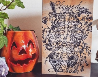 May include: A tan card with a black and white illustration of a human skeleton with flowers and vines growing from it. The text "Blessed" is at the top of the card and the text "Unchain" is at the bottom.