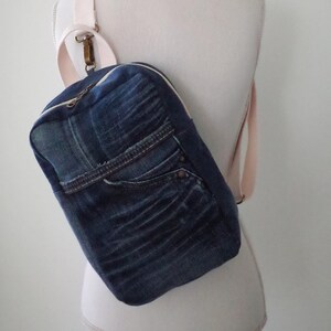 May include: A denim backpack with a light pink strap. The backpack is made from recycled denim and has a unique patchwork design.