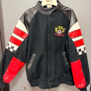 Può includere: Giacca college nera con maniche e colletto in pelle. Le maniche presentano strisce rosse e bianche e un motivo a scacchi sui polsini. La giacca presenta la scritta "MOM 'N' POP'S" e un logo con bandiera da corsa.