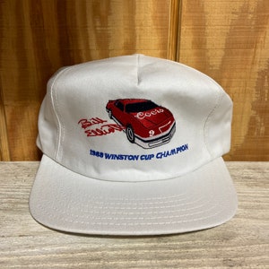 Puede incluir: Gorra de béisbol blanca con un coche de carreras rojo bordado en la parte delantera. El coche tiene el número 9 y el texto "Coo Coo" en él. El texto "Bill Elliott 1988 Winston Cup Champion" está bordado debajo del coche.