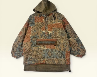 May include: A long-sleeve pullover hoodie featuring a patchwork pattern in shades of brown, orange, and blue. The garment includes a hood, a front kangaroo pocket with the text "courmayeur" embroidered on a brown patch, and a drawstring hem.