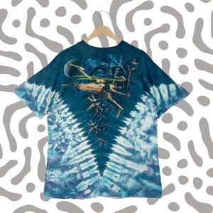 Puede incluir: Camiseta te&ntilde;ida con un dise&ntilde;o de Star Wars. El dise&ntilde;o incluye cazas X-wing, un planeta y el casco de Darth Vader sobre un fondo espacial. La camiseta tiene un patr&oacute;n de espiral azul y blanco.