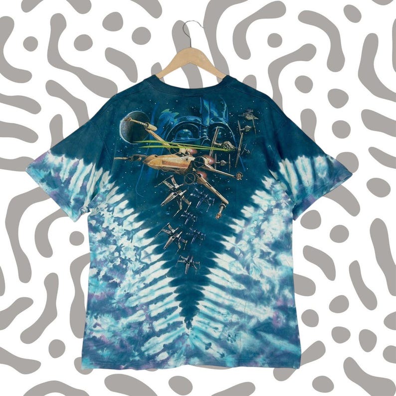 Puede incluir: Camiseta te&ntilde;ida con un dise&ntilde;o de Star Wars. El dise&ntilde;o incluye cazas X-wing, un planeta y el casco de Darth Vader sobre un fondo espacial. La camiseta tiene un patr&oacute;n de espiral azul y blanco.