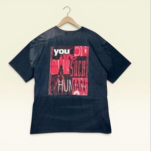 May include: A black short-sleeve t-shirt featuring a rectangular graphic on the back. The graphic contains red and black abstract patterns with the white and black text that reads: you are SUCH A HUMAN. The shirt is displayed on a wooden hanger.