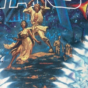 Puede incluir: Una camiseta gr&aacute;fica de Star Wars con una vibrante ilustraci&oacute;n de Luke Skywalker empu&ntilde;ando un sable de luz, con la Princesa Leia, C-3PO y R2-D2 de fondo. La palabra "STAR WARS" est&aacute; en la parte superior en azul y blanco.