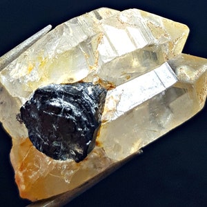 May include: A clear quartz crystal with a black hematite inclusion. The quartz crystal is double terminated and has a natural, rough surface.