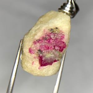 May include: A small, rough, white stone pendant with a silver bail. The stone has a cluster of pink ruby crystals embedded in it.