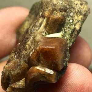 May include: A close-up of a brown and tan rock with several brown crystals. The crystals have a sharp, geometric shape.