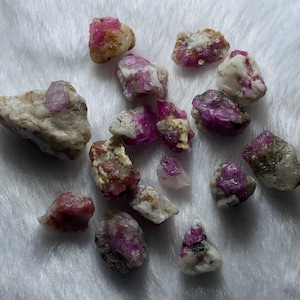 May include: A collection of raw, unpolished mineral stones featuring a mix of opaque white and translucent deep pink to magenta crystalline inclusions. These irregular, jagged rock fragments vary in size and display natural textures throughout.