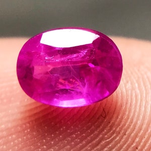 May include: A vibrant pink oval-shaped gemstone with a smooth, polished surface.