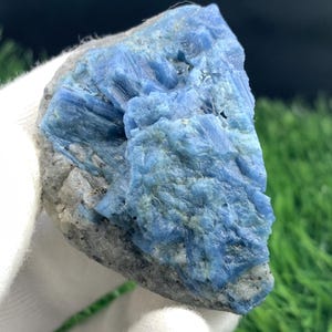 Puede incluir: Primer plano de un espécimen mineral natural en bruto. La piedra presenta un llamativo color azul con una estructura cristalina, sobre una matriz gris. El mineral es sostenido por una mano enguantada.