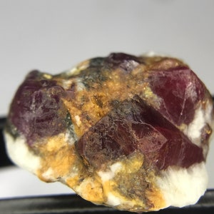 May include: A close-up of a red ruby crystal embedded in a matrix of white and brown rock. The ruby has a deep red color and is surrounded by a white and brown matrix.