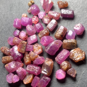 May include: A collection of raw ruby gemstones in various shapes and sizes. The gemstones display a range of colors from deep pink to reddish-brown. Some have a rough, natural texture, while others have a more polished appearance.