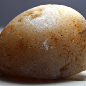 May include: A smooth, light brown agate stone with a white center. The stone has a rough, textured surface.