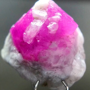 May include: A pink and white crystal with a rough, natural texture. The crystal is a vibrant pink color and has a pointed shape.