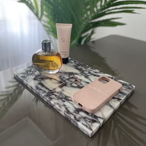 Könnte beinhalten: Ein weißes Marmortablett mit einer rosa Handyhülle, auf der der Name "sabi" steht. Auf dem Tablett befinden sich eine Parfümflasche und eine Tube Lotion.