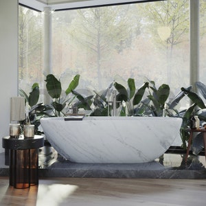 Op de afbeelding: Een wit marmeren bad met een modern ontwerp staat in een badkamer met grote ramen en weelderige groene planten. Het bad is vrijstaand en heeft een strakke, minimalistische uitstraling.