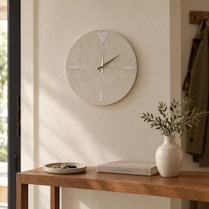 May include: A circular wall clock with a textured beige stone-like face, featuring four silver-toned markers at the cardinal positions and thin gold-colored hour, minute, and second hands. The clock has a clean, flat design with no numerals.