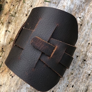 May include: A brown leather bracelet with a woven design. The bracelet is made of thick, durable leather and has a rustic look.