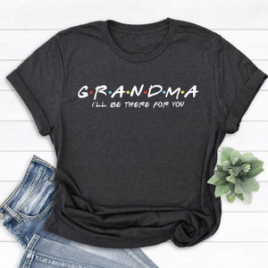 以下が含まれることがあります： 暗いグレーのTシャツに「G.R.A.N.D.M.A. I'LL BE THERE FOR YOU」という白い文字が書かれています。文字はカラフルな点で区切られています。