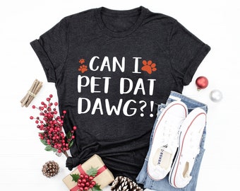May include: A dark grey t-shirt with white text that reads "CAN I PET DAT DAWG?!" with two red paw prints on either side of the text.