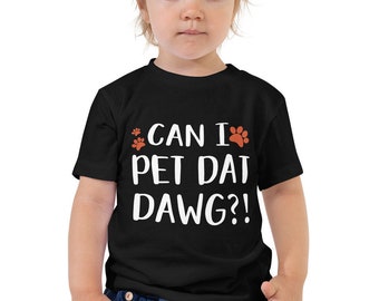 May include: Black toddler t-shirt with the phrase "CAN I PET DAT DAWG?!" in white text. The design includes orange paw prints above and to the right of the text. The shirt is a short-sleeved crew neck.