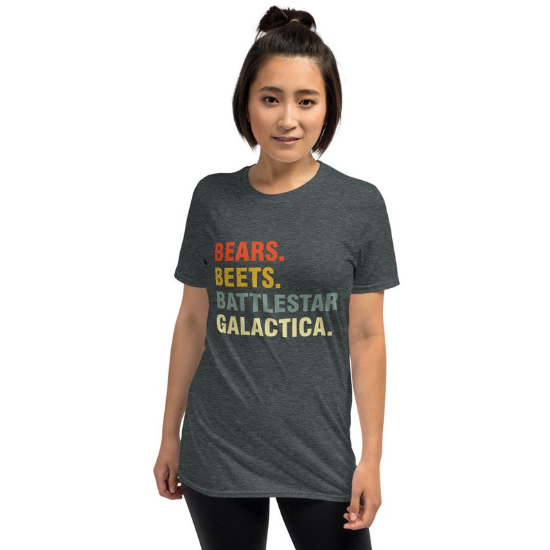 Pu&ograve; includere: Una t-shirt grigio scuro melange con il testo "BEARS. BEETS. BATTLESTAR GALACTICA." stampato in stile retr&ograve; con colori rosso, arancione, giallo e verde.