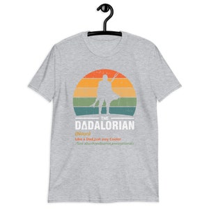 May include: A grey t-shirt with a retro design. It features the text "THE DADALORIAN" and a silhouette of a figure in front of a sunset. The text below reads "Like a Dad, just way Cooler / See also: handsome, exceptional/".