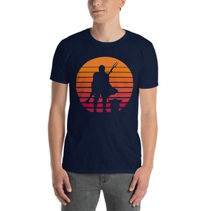 May include: A navy blue t-shirt with a retro sunset graphic featuring a silhouette of a Mandalorian with a spear and Grogu.