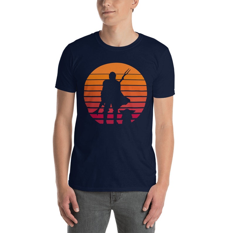 May include: A navy blue t-shirt with a retro sunset graphic featuring a silhouette of a Mandalorian with a spear and Grogu.