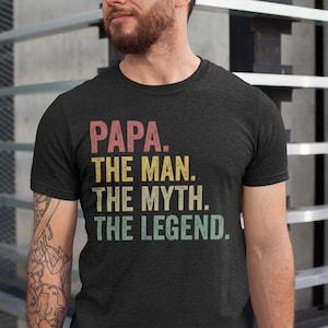 Könnte beinhalten: Ein dunkelgraues T-Shirt mit einer Grafik im Vintage-Stil, auf dem "PAPA. THE MAN. THE MYTH. THE LEGEND." steht.