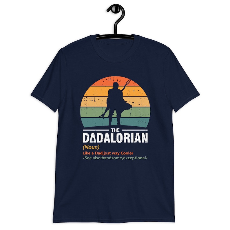 May include: Dark blue t-shirt with a retro sunset design and a silhouette of a figure holding a weapon. The text reads "THE DADALORIAN" with a definition below. A unique graphic tee for fans of the series.