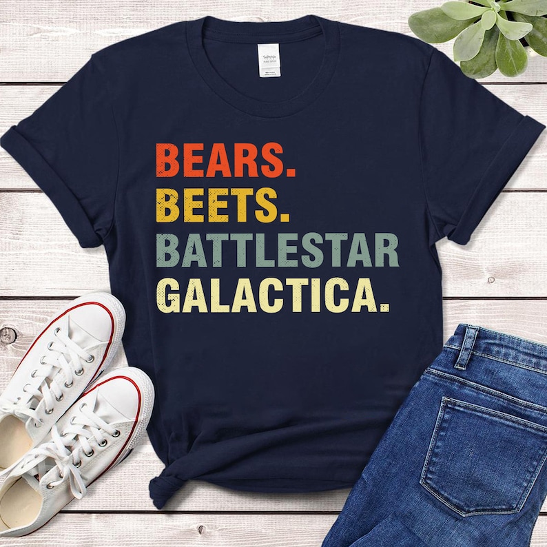 Pu&ograve; includere: Una maglietta blu navy con una grafica in stile vintage che recita "Bears. Beets. Battlestar Galactica."