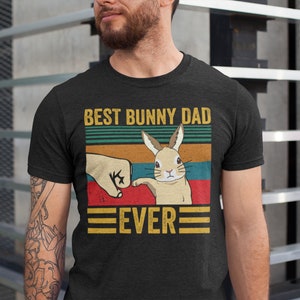 May include: A black t-shirt with a vintage-style graphic of a bunny rabbit giving a fist bump. The text "Best Bunny Dad Ever" is printed on the shirt.