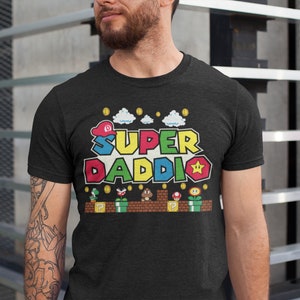 May include: A black t-shirt with a colorful graphic of a video game character. The graphic says "Super Daddi" with a star and coins.