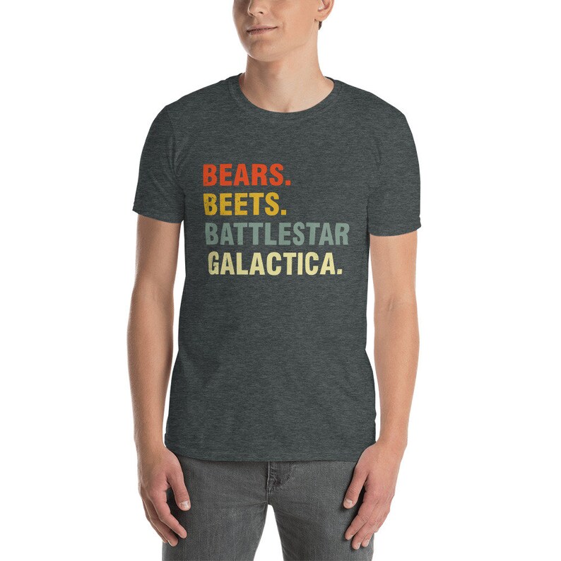 Pu&ograve; includere: Una t-shirt grigio scuro melange con il testo "BEARS. BEETS. BATTLESTAR GALACTICA." stampato in un font in stile retr&ograve; con colori rosso, arancione, giallo e verde.