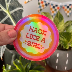 May include: A holographic sticker with a rainbow background and the text "Hack Like A Girl" in white.