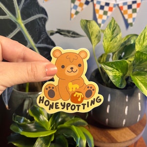 May include: A yellow sticker with a cartoon brown bear holding a pot of honey. The text "HONEYPOTTING" is written below the bear.