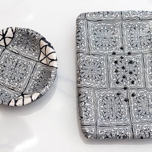 May include: Two ceramic dishes with a black and white geometric pattern. The smaller dish is round and the larger dish is rectangular.